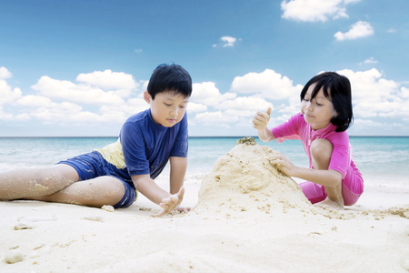 Picture of two little children looks happy while making sand castle on the beachの写真素材