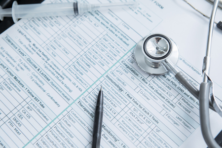 Top view of patient medical form with syringe, stethoscope and pen on the table