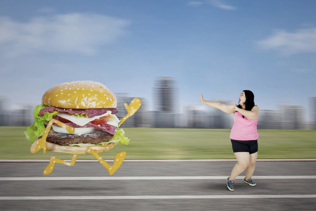 Picture of fat woman escaping from a burger while running on the trackの写真素材