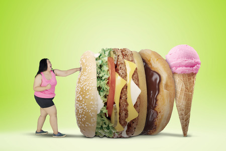 Diet concept. Overweight woman wearing sportswear while fighting with unhealthy foods. Shot with green screenの写真素材