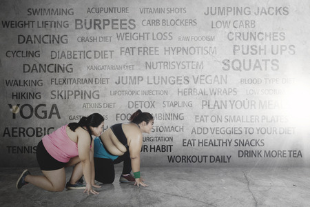 Concept of dieting and weight loss. Two overweight women ready to run while kneeling togetherの写真素材