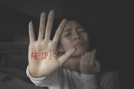 Image of abused woman showing help word on her palm while being strangled by her husband in the dark roomの写真素材