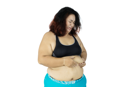 Sad obese woman wearing sportswear while pinching her belly fat, isolated on white backgroundの写真素材