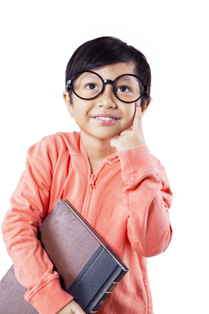 Picture of cute schoolgirl carrying a book while thinking an idea, isolated white backgroundの写真素材