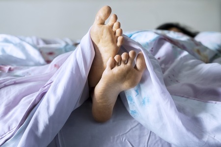 Close up of young woman feet sticking out from under a blanket during resting on the bed