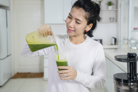 Portrait of happy woman pouring healthy juice into a glass while standing in the kitchenの写真素材