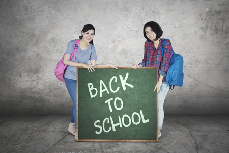 Image of two female college students holding a chalkboard with text of back to schoolの写真素材