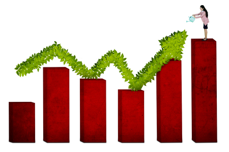 Happy businesswoman is standing above growth chart while watering a tree shaped upward arrow, isolated on white backgroundの写真素材