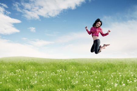 Carefree Asian woman making a big jump on meadow. Summer or Spring conceptの写真素材