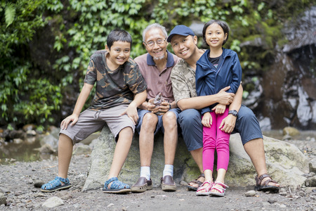 Picture of Asian family smiling at the camera while sitting on the stone and taking a selfie photo togetherの写真素材