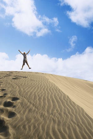 Low angle view of a handsome preteen enjoying his holiday while jumping under blue sky. Shot on the beachの写真素材