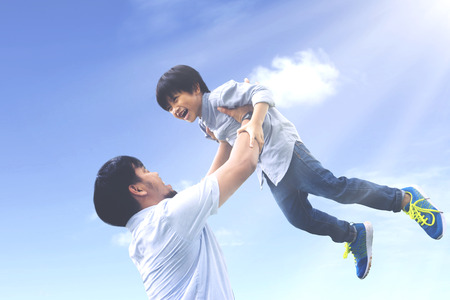 Portrait of young father lifting his son with happy expression under clear skyの写真素材