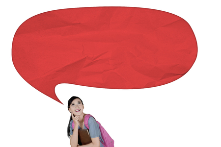 Caucasian female student thinking an idea while looking at an empty cloud bubble, isolated on white...