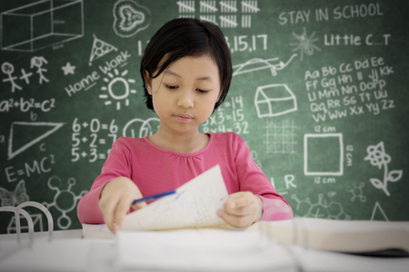 Picture of cute schoolgirl doing an exam while sitting in the classroom with scribbles on the chalkboardの写真素材