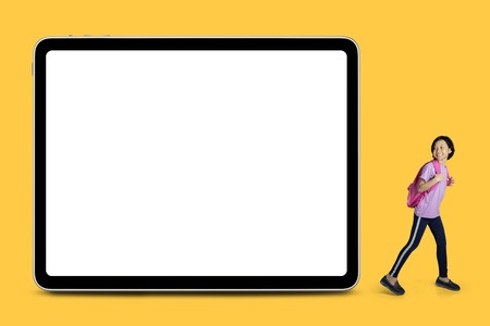 Portrait of happy schoolgirl looking at a blank whiteboard while standing with yellow backgroundの写真素材