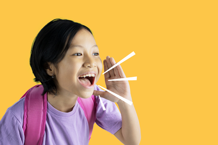 Picture of Asian schoolgirl looks happy while shouting through her hand. Shot with yellow screenの写真素材