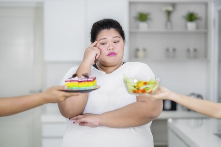 Overweight woman does not know what to choose between rainbow cake and salad