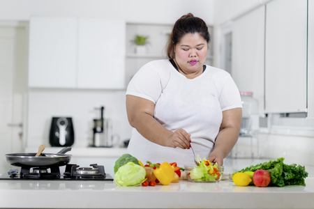 Overweight woman preparing fruits and vegetables salad in kitchenの写真素材