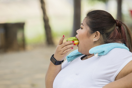 Overweight woman eating doughnuts while resting during morning exerciseの写真素材
