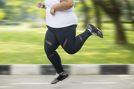 Feet of obese woman doing exercise while sprinting on the asphalt road with fast motionの写真素材