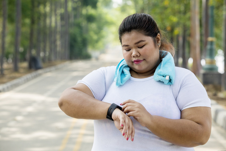 Picture overweight woman wearing her smartwatch before doing a jogging on the road