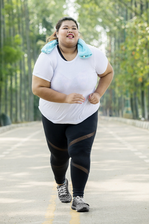 Portrait of obese woman wearing sportswear while running on the roadの写真素材