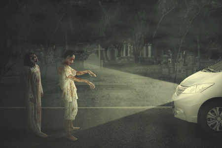 Halloween horror concept. Two ghosts stopping a car at night time. Shot with grave backgroundの写真素材