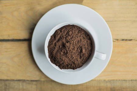 Top view of a cup full of ground coffee on the saucer over wooden table, shot in the studioの写真素材
