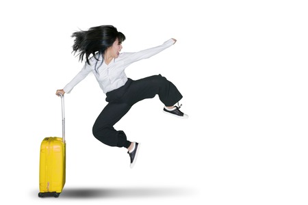 Cheerful young businesswoman jumping in the studio while holding a luggage for travel. Isolated on white backgroundの写真素材