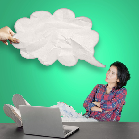 Picture of female college student studying with laptop while looking at a blank cloud bubbleの写真素材