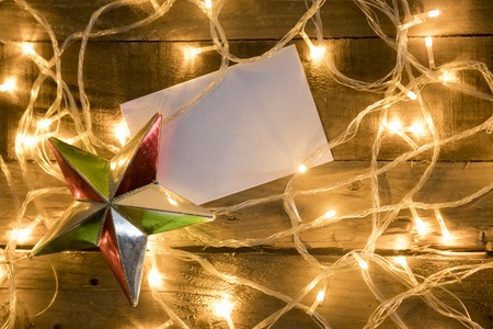 Christmas star ornament with blank paper and christmas lights on vintage wooden backgroundの写真素材