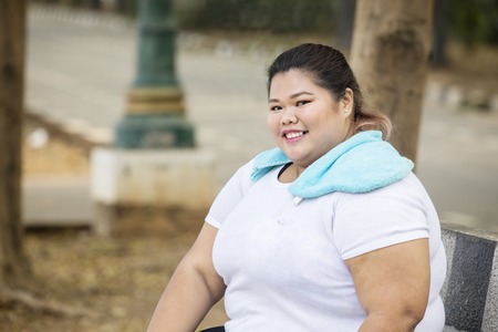 Picture of fat woman wearing sportswear while smiling at the camera and sitting in the park