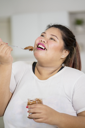 Closeup of obese woman enjoying chocolate cream with a spoon at homeの写真素材