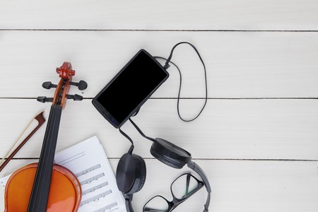 Top view of brown violin with smartphone and headphone on the wooden table
