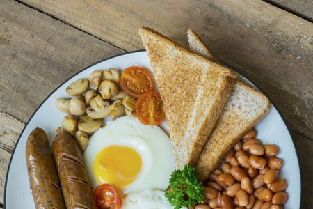 Top view of English breakfast served with toast, egg, sausage, beans and mushroom on the plate