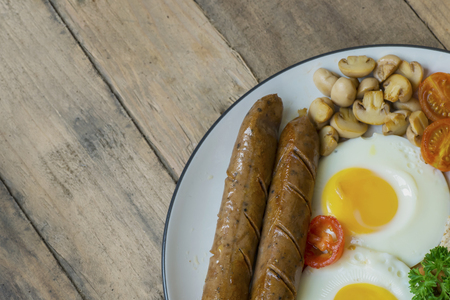 Top view of tasty sausage with fried egg and mushroom on the plate. Shot on the wooden tableの写真素材