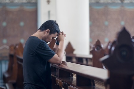 Picture of young man standing with clasped hands while praying to GOD in the churchの写真素材