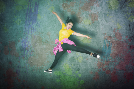 Picture of young female dancer jumping high and dancing in the studio with colorful concrete backgroundの写真素材