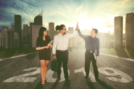 Diversity of business people clapping hands while standing above number 2019 on the road in sunlight backgroundの写真素材