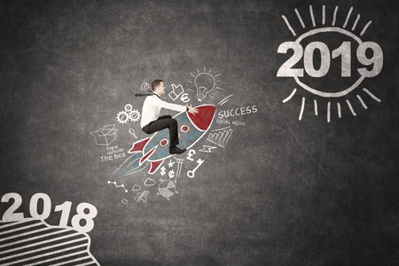 Picture of a Caucasian businessman flying toward number 2019 with a rocket in blackboard backgroundの写真素材