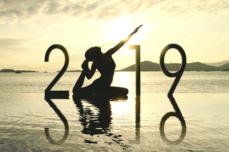 Picture of silhouette woman doing yoga on the beach with number 2019 at sunset time