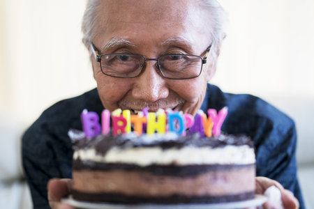 Portrait of happy old man holding chocolate birthday cake with colorful candlesの写真素材