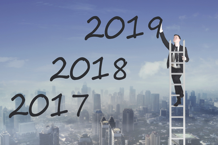 American businessman standing on the ladder while writing number 2019 in the sky