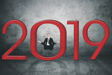 American businessman doing meditation while levitating with stones shaped number 2019