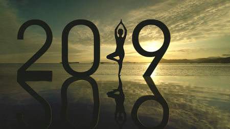 Silhouette of unknown woman exercising yoga on the beach while standing with number 2019 at sunset...