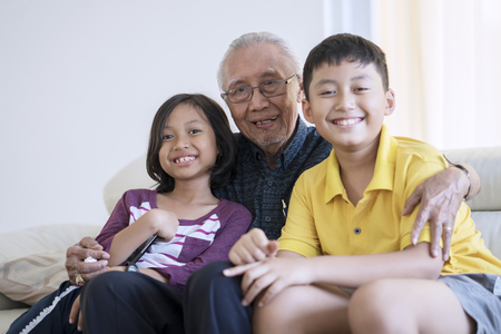 Portrait of happy senior man and his grandchildren smiling at the camera while sitting on the sofa...
