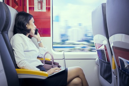 Young business woman speaking on a mobile phone while working with a laptop in the airport trainの写真素材