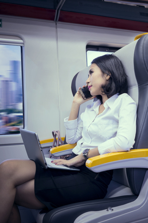 Female worker talking on a mobile phone while working with a laptop in the airport trainの写真素材