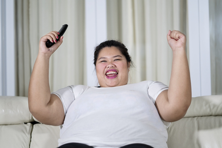 Picture of obese woman watching television with happy expression while sitting on the couchの写真素材