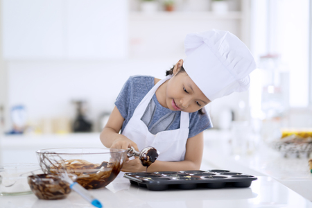 Photo of cute little chef preparing chocolate dough on the mold to make cookie in the kitchen at homeの写真素材